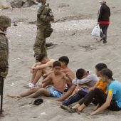 Miembros del Ejército de Tierra vigilan a un grupo de inmigrantes menores que han logrado cruzar uno de los espigones fronterizos de Ceuta 