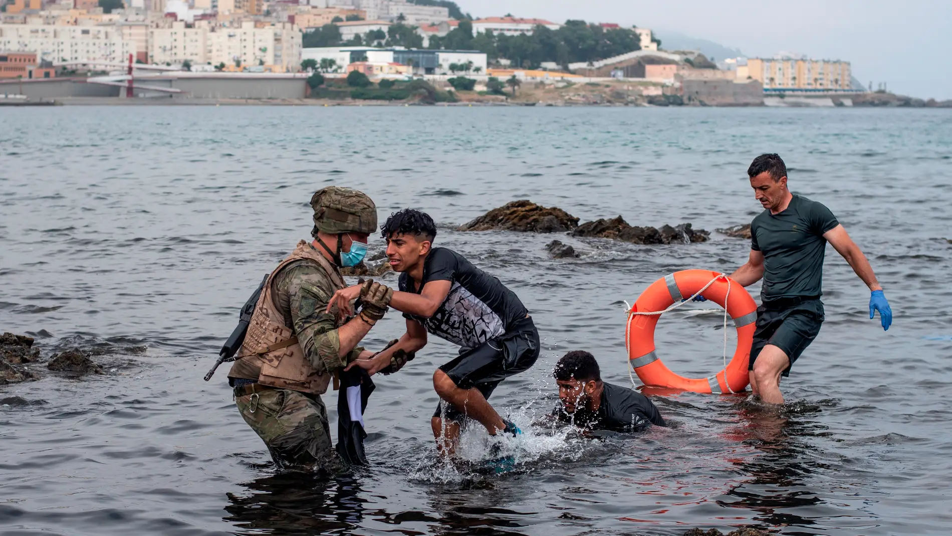 Un miembro del Ejército ayuda a menores migrantes llegados a Ceuta.
