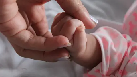 Imagen de archivo de una madre sujetando la mano de su bebé. Imagen de archivo de una madre sujetando la mano de su bebé.