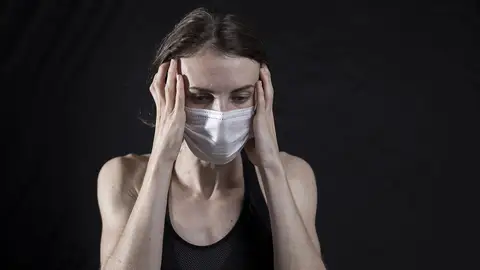 Persona con mascarilla y un fuerte dolor de cabeza Persona con mascarilla y un fuerte dolor de cabeza