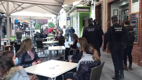 La policía local patrulla por una calle con veladores La policía local patrulla por una calle con veladores