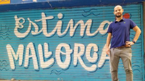 Javi Torrado, socio de Melicotó, posa frente a una barrera de Els Geranis (Palma) decorada con frases como &quot;Avui fora nirvis&quot; o &quot;Bon dia tot lo dia&quot;