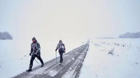 Dos personas caminan por una carretera nevada en el norte de España Dos personas caminan por una carretera nevada en el norte de España