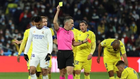 El colegiado Jaime Latre muestra tarjeta amarilla al centrocampista brasile&ntilde;o del Real Madrid, Carlos Henrique Casemiro (i), tras realizar una entrada sobre el delantero del C&aacute;diz, Iv&aacute;n Alejo