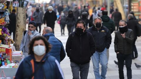 Varias personas pasean por la calle con mascarilla.