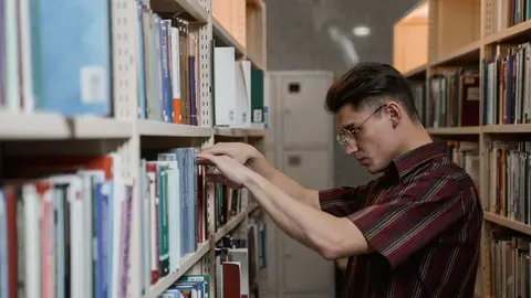 Joven buscando un libro en una biblioteca Joven buscando un libro en una biblioteca