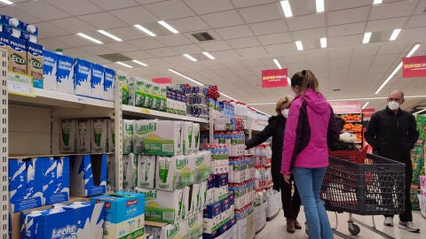 Varias personas compran leche en un supermercado de Madrid, donde algunas estanter&iacute;as permanecen vac&iacute;as a causa de la huelga indefinida de transporte
