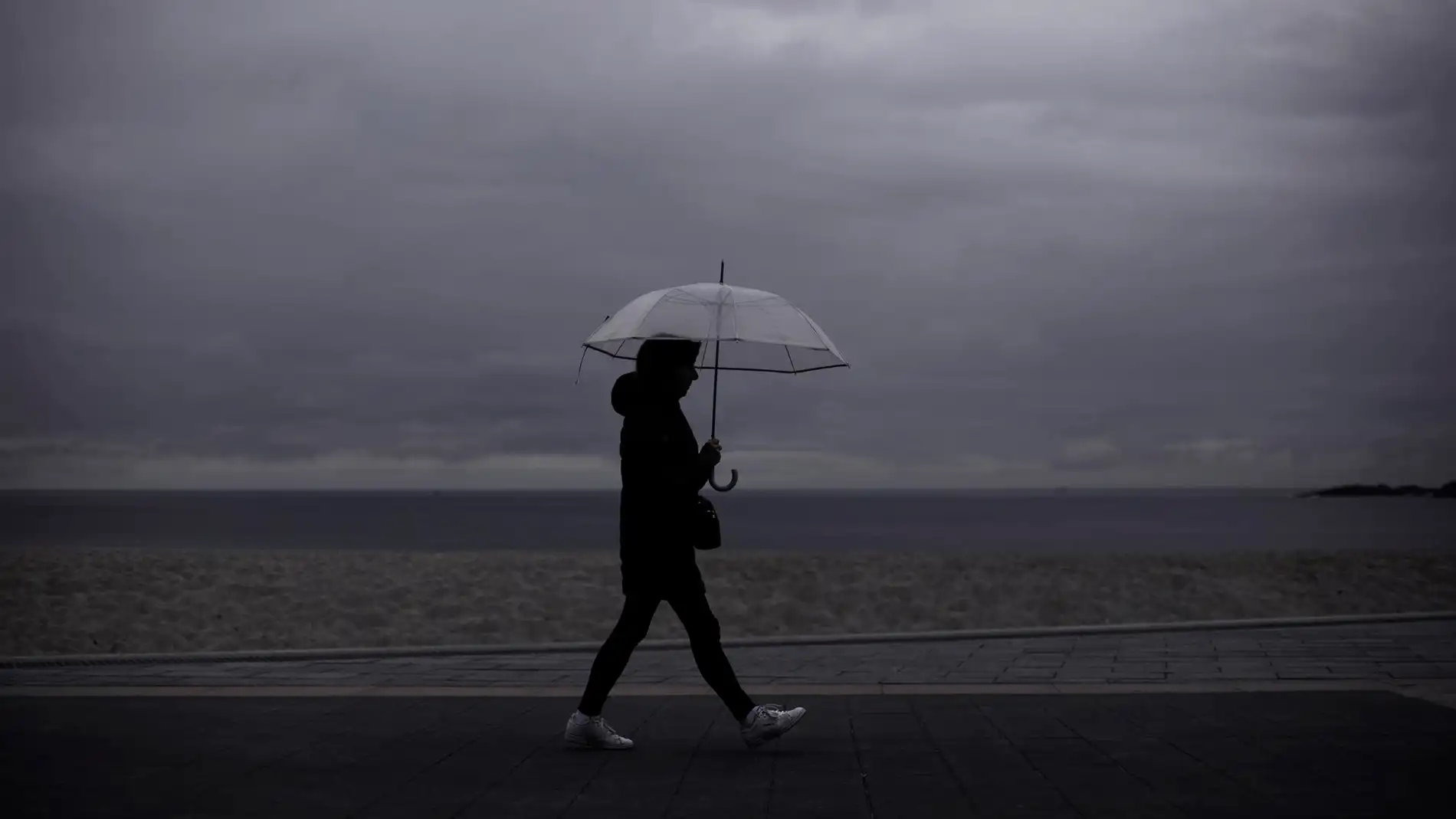 Una mujer camina por una playa mientras llueve. / Efe Una mujer camina por una playa mientras llueve. / Efe