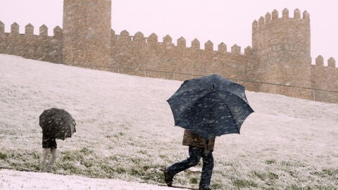 Dos personas se protegen de la nieve junto a la muralla de &Aacute;vila/ EFE