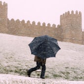 Dos personas se protegen de la nieve junto a la muralla de Ávila