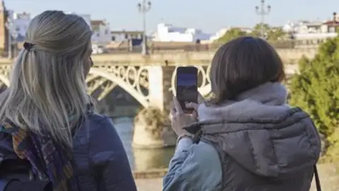 Dos turistas fotografían el puente de Triana