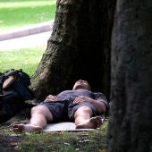 Un joven descansa resguardado del calor en el Campo de San Francisco, en Oviedo