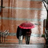 Dos personas pasean protegiéndose de la lluvia.