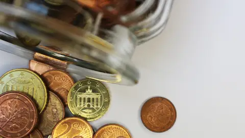 Imagen de archivo de un bote de cristal volcado con monedas de céntimo en su interior