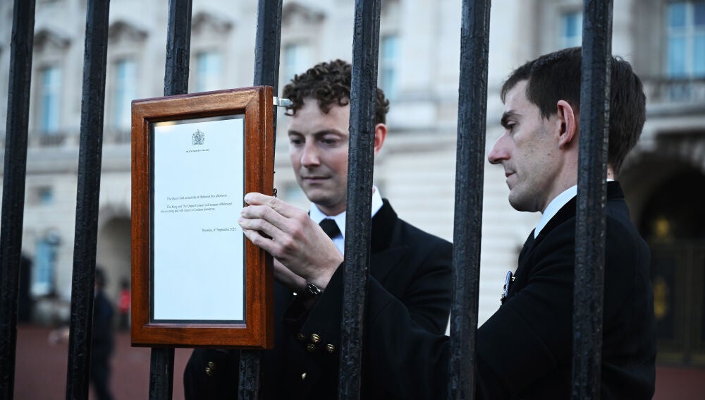 Dos funcionarios británicos cuelgan el comunicado oficial sobre la muerte de Isabel II en Buckingham Palace