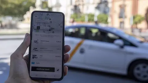 Imagen de un usuario con su teléfono móvil consultando los VTC ante una parada de taxis Imagen de un usuario con su teléfono móvil consultando los VTC ante una parada de taxis