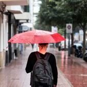 Una mujer se protege de la lluvia con un paraguas mientras camina por una calle.