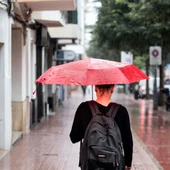 Una mujer se protege de la lluvia con un paraguas mientras camina por una calle de Córdoba Una mujer se protege de la lluvia con un paraguas mientras camina por una calle de Córdoba
