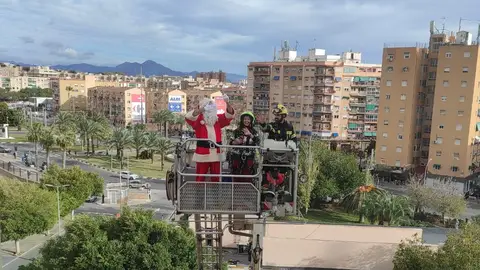 Papá Noel llega a la Unidad de Oncología pediatrica de Alicante ayudado por los bomberos del SPEIS Papá Noel en la cesta del vehículo de los bomberos