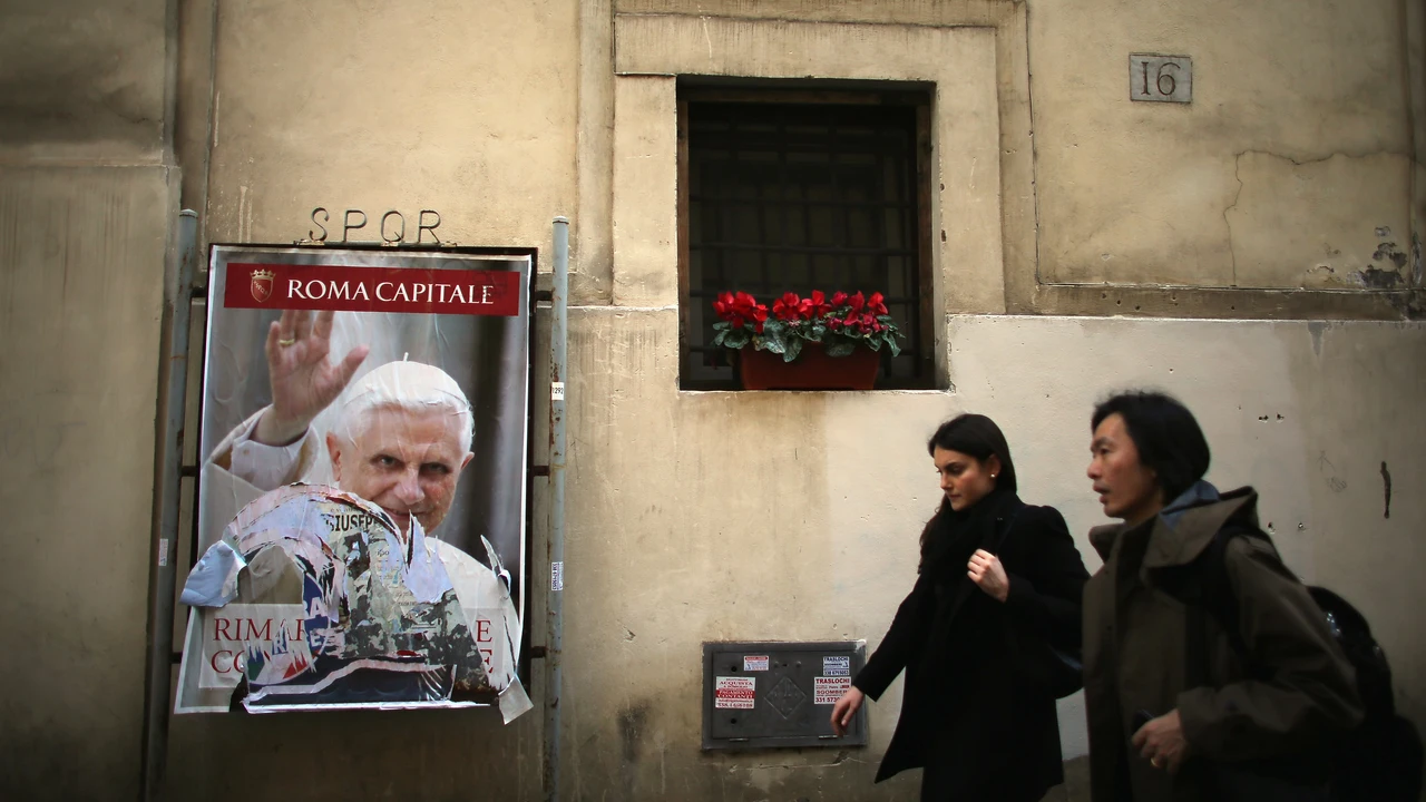 Unas personas caminan junto a un poster de Benedicto XVI en una pared de la Ciudad del Vaticano en marzo de 2013