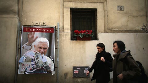 Unas personas caminan junto a un poster de Benedicto XVI en una pared de la Ciudad del Vaticano en marzo de 2013
