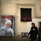 Unas personas caminan junto a un poster de Benedicto XVI en una pared de la Ciudad del Vaticano en marzo de 2013