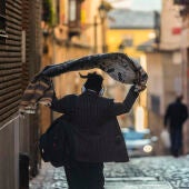 Una persona se echa una prenda de abrigo sobre los hombros mientras camina por una calle de Toledo. 