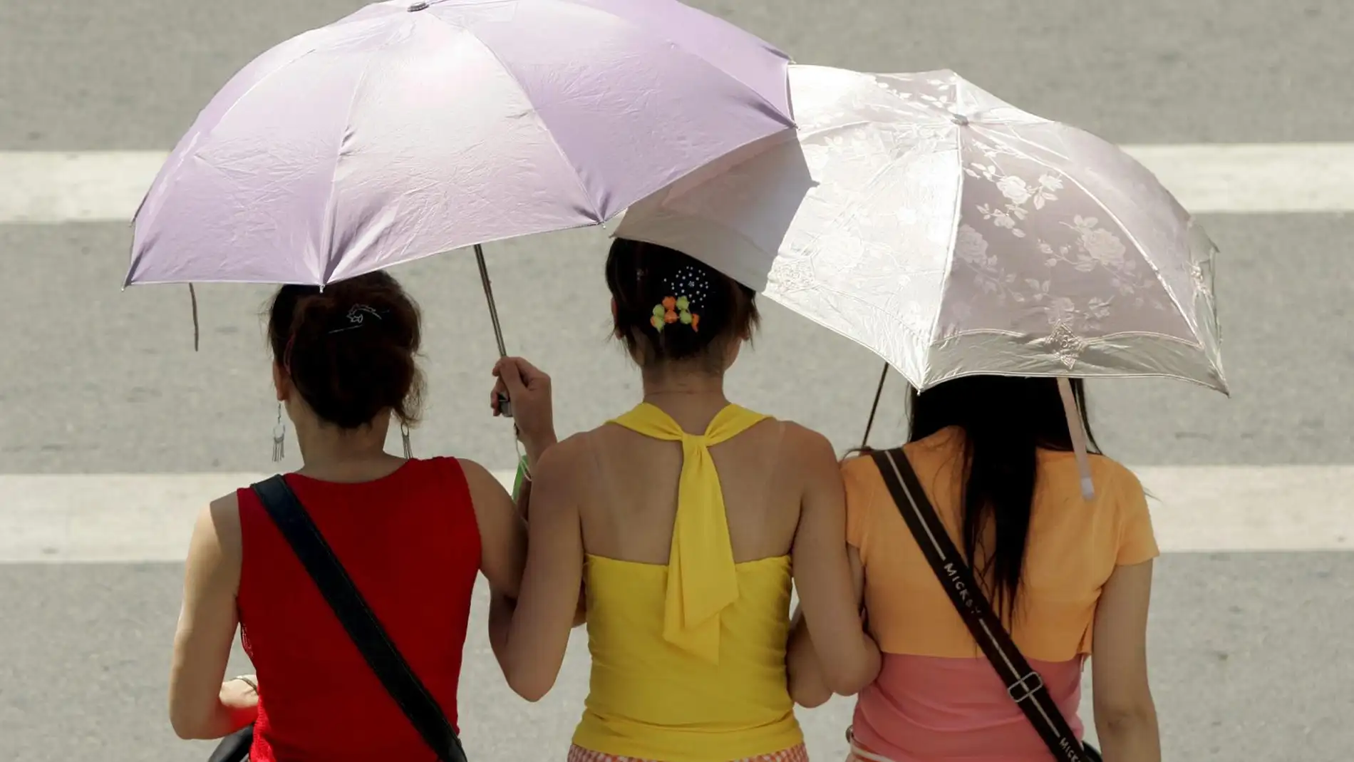 Fotografía de archivo de tres jóvenes que se protegen del sol con un paraguas