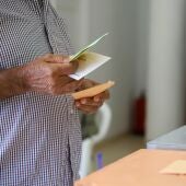 Un hombre sostiene sus papeletas de votación ante las urnas de la mesa en el colegio electoral.