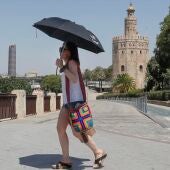 Una turista se cubre con un paraguas mientras camina junto a la Torre del Oro de Sevilla.