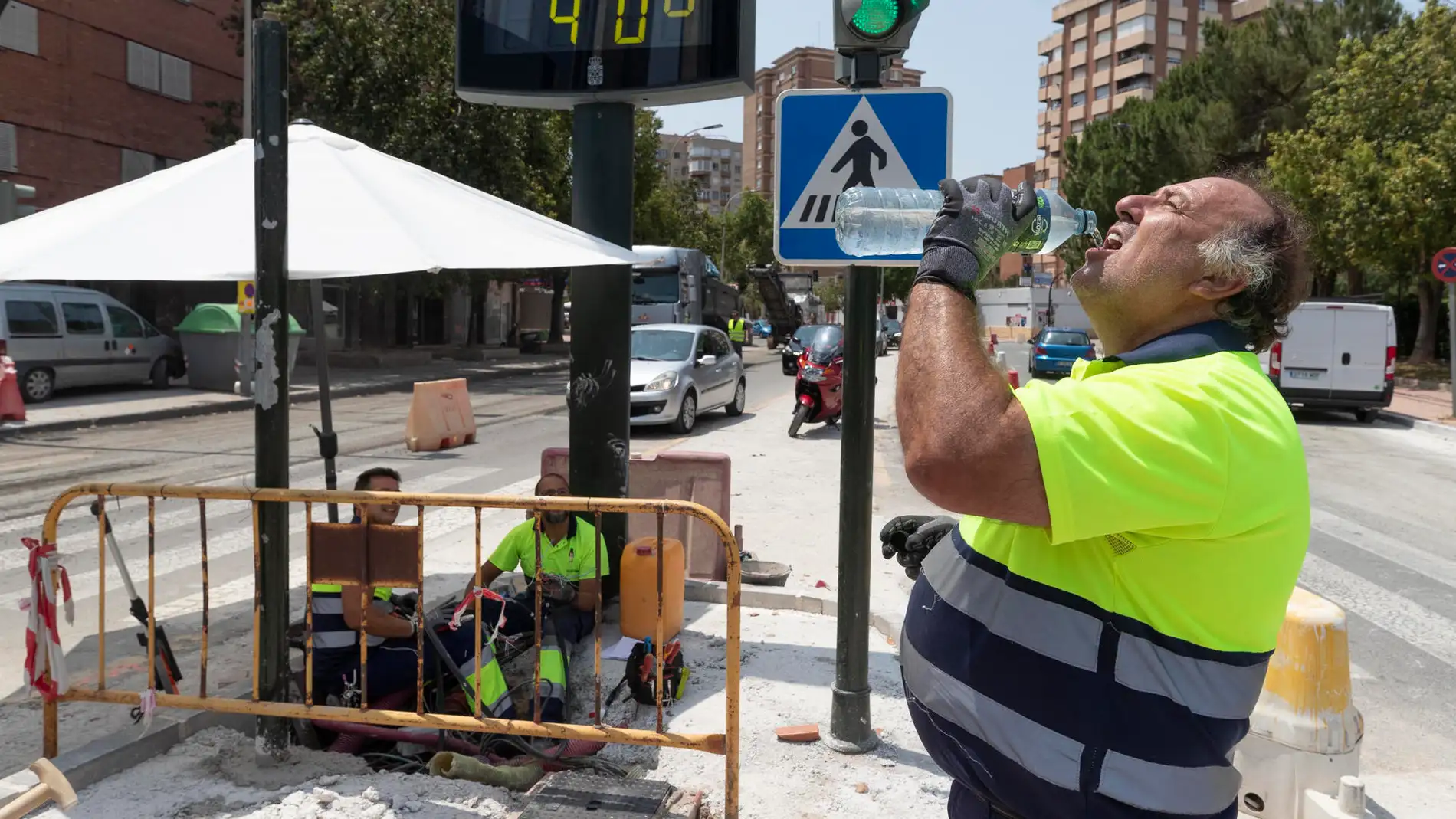 Un trabajador de la construcción combate el calor con agua junto a un termómetro que marca 40 grados este martes en la avenida de la Fama de Murcia.