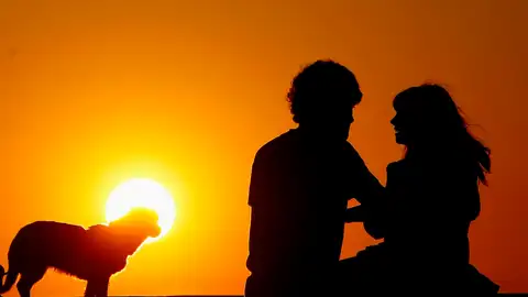 Una pareja observa con su perro la puesta de sol en San Sebastián Una pareja observa con su perro la puesta de sol en San Sebastián
