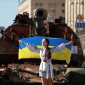  Una mujer sostiene la bandera nacional de Ucrania mientras posa para una fotografía frente a vehículos militares blindados rusos dañados