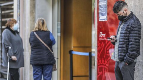 Archivo - Un joven mira su teléfono móvil mientras espera para entrar en una oficina de empleo en València. 