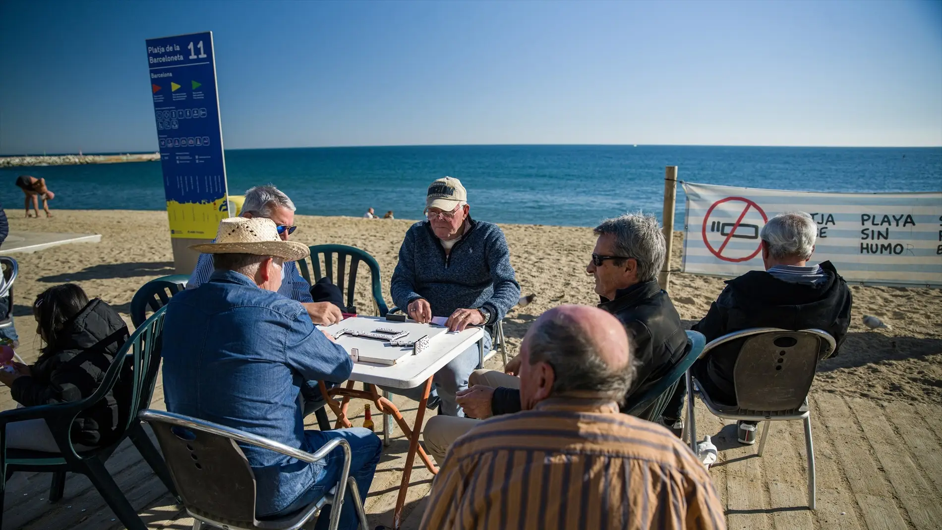 Unos hombres juegan al dominó en la playa de la Barceloneta.