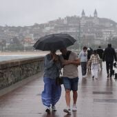 Dos personas se protegen de la lluvia con un paraguas en la playa de Ondarreta, en San Sebastián.
