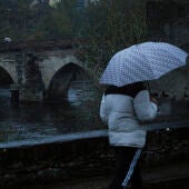 Una persona se protege de la lluvia junto al Puente Romano de Lugo