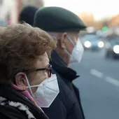 Una pareja de ancianos con mascarillas esperando para cruzar una calle. Una pareja de ancianos con mascarillas esperando para cruzar una calle.