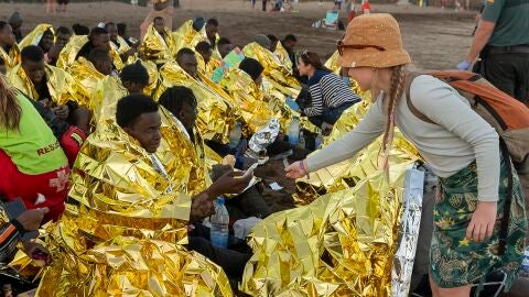 Cincuenta cuatro inmigrantes de origen subsahariano, entre ellos siete mujeres y una niña, han llegado a bordo de una lancha neumática a la playa de La Garita, en Arrieta (norte de Lanzarote). En la imagen, una joven ofrece una barra de chocolate a uno de los recién llegados