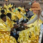 Cincuenta cuatro inmigrantes de origen subsahariano, entre ellos siete mujeres y una niña, han llegado a bordo de una lancha neumática a la playa de La Garita, en Arrieta (norte de Lanzarote). En la imagen, una joven ofrece una barra de chocolate a uno de los recién llegados