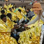 Cincuenta cuatro inmigrantes de origen subsahariano, entre ellos siete mujeres y una niña, han llegado a bordo de una lancha neumática a la playa de La Garita, en Arrieta (norte de Lanzarote). En la imagen, una joven ofrece una barra de chocolate a uno de los recién llegados Cincuenta cuatro inmigrantes de origen subsahariano, entre ellos siete mujeres y una niña, han llegado a bordo de una lancha neumática a la playa de La Garita, en Arrieta (norte de Lanzarote). En la imagen, una joven ofrece una barra de chocolate a uno de los recién llegados