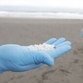 Un operario coge con la mano pellets de plástico, en la playa Otur en Valdés, Asturia