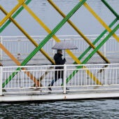 Una mujer con paraguas atraviesa el puente de San Sebastián en Avilés