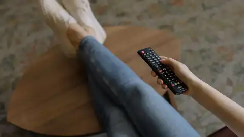 Una persona cambia de canal con el mando a distancia de la televisión Una persona cambia de canal con el mando a distancia de la televisión
