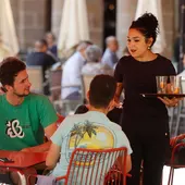 Una trabajadora de hostelería atiende a unos clientes. Una trabajadora de hostelería atiende a unos clientes.