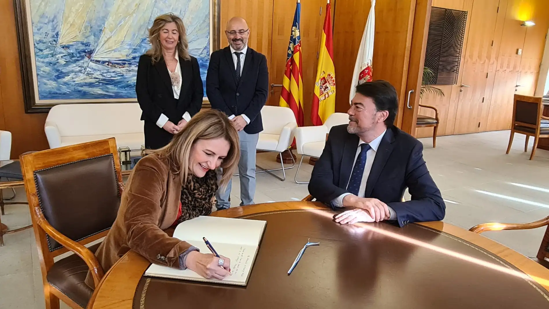La consellera Nuria Montes firma en el libro de honor del ayuntamiento ante el alcalde Luis Barcala