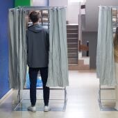 Dos personas ejercen su derecho a voto en una cabina en un colegio electoral