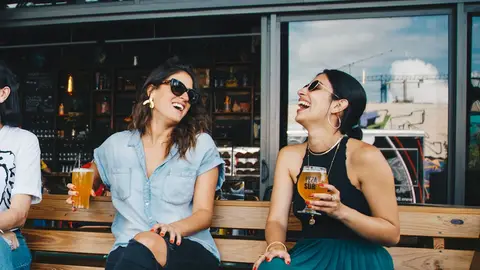 Dos amigas se ríen a carcajadas mientras toman unas cervezas