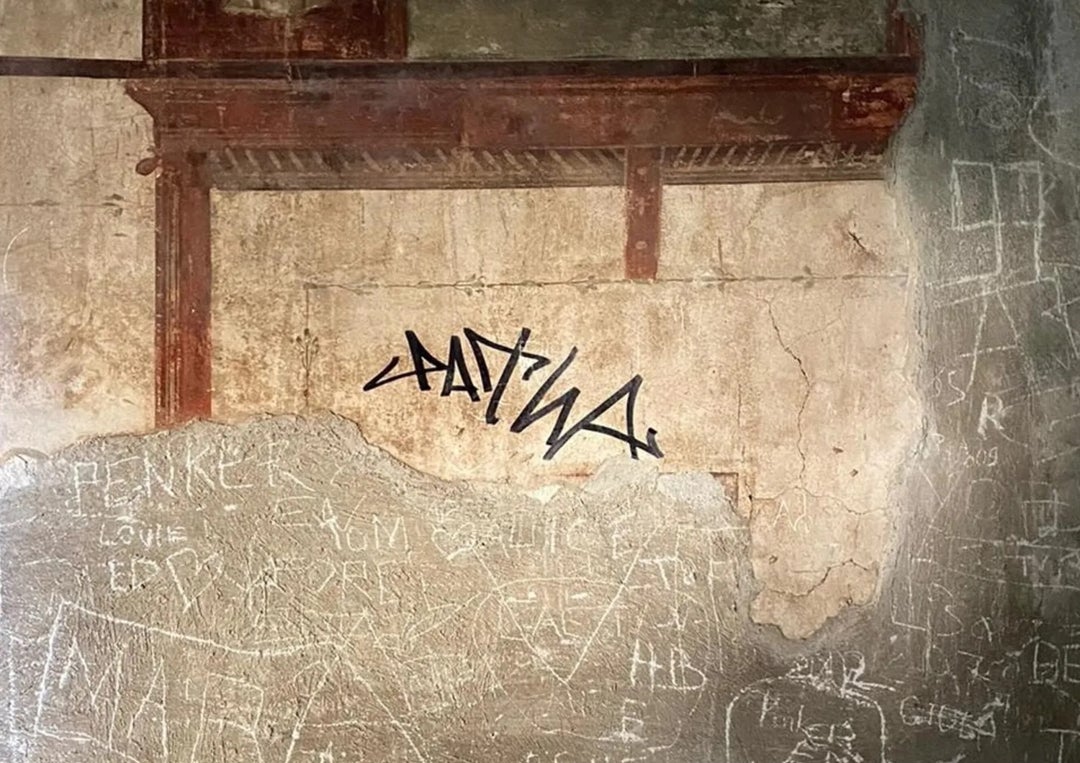 Un turista garabatea su firma con rotulador en una pared con frescos en la antigua ciudad de Herculano Un turista garabatea su firma con rotulador en una pared con frescos en la antigua ciudad de Herculano
