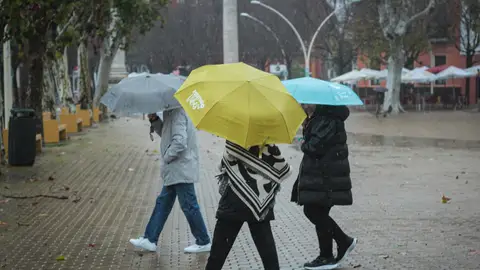 Tres personas se protegen de la lluvia con paraguas en una imagen de archivo. Tres personas se protegen de la lluvia con paraguas en una imagen de archivo.